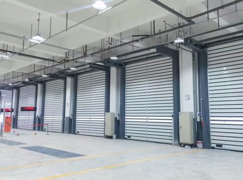 Several high-speed aluminum roll-up doors mounted on the walls of a logistics plant.